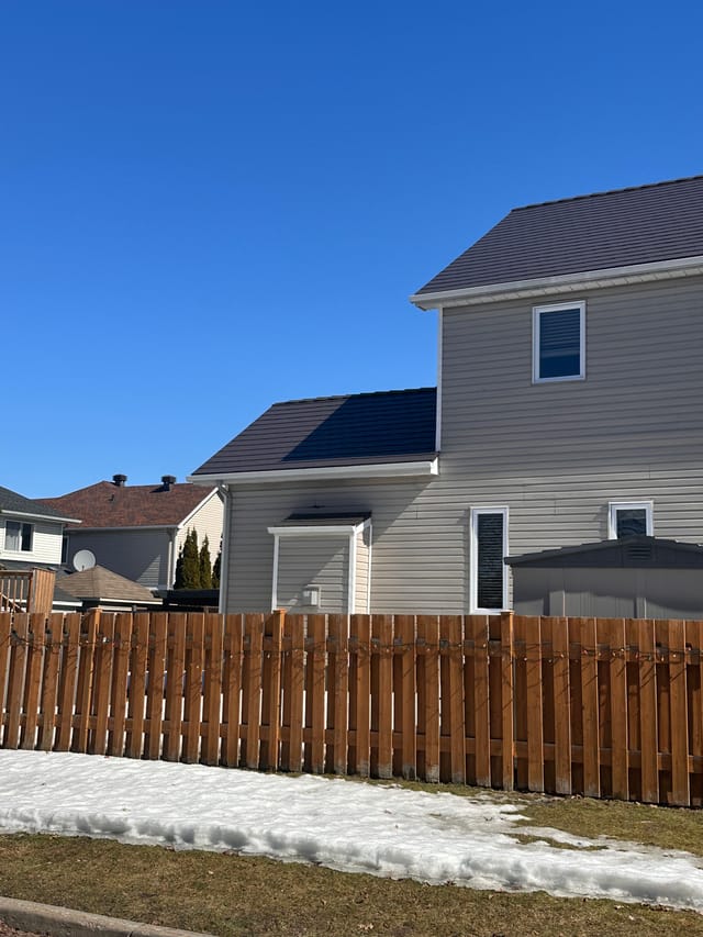 Tudor Brown Interlock aluminum slate metal roof on a two-storey suburban home in Ottawa, viewed from rear-left with a wooden fence in the foreground.