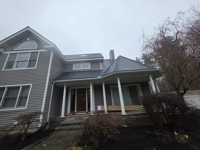 Two-story Victorian home in Pelham NH with deep charcoal Interlock aluminum slate metal roof, covered front porch with white columns, dormer, skylight, and chimney.