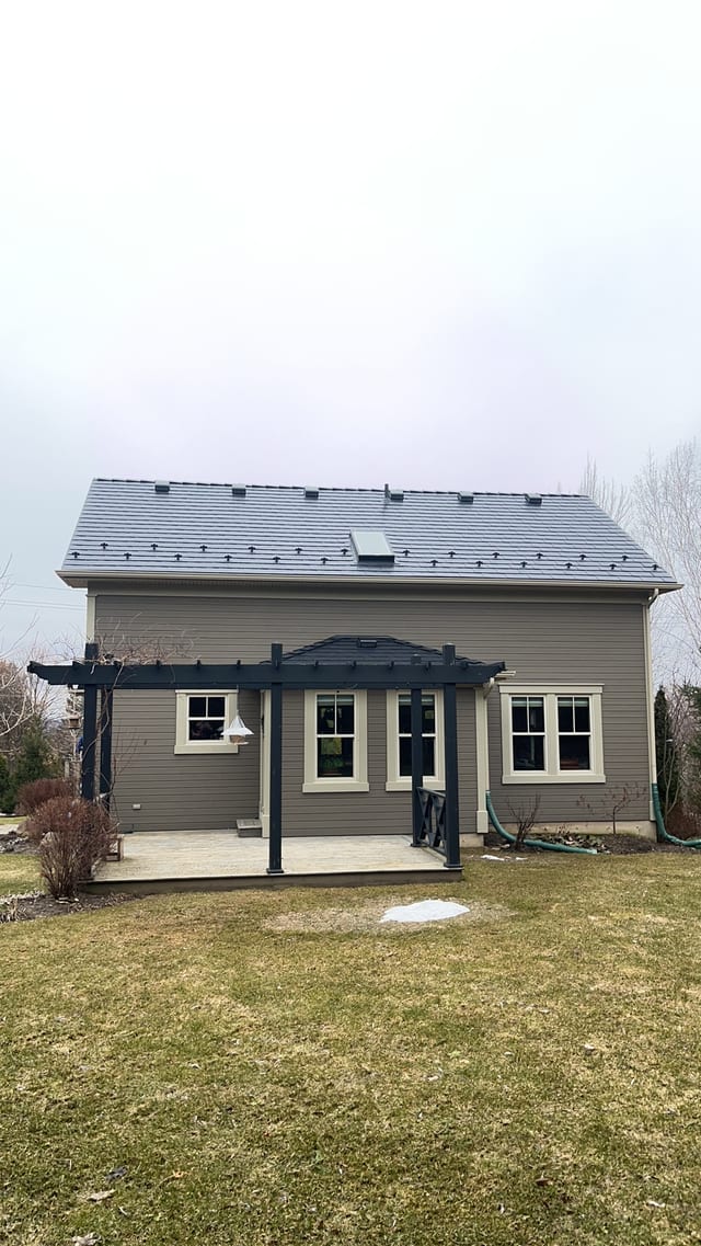 Rear elevation of a Craftsman-style home in Ravenna, ON featuring Interlock black aluminum slate metal roofing with snow guards, skylights, and a dark pergola over a rear patio.