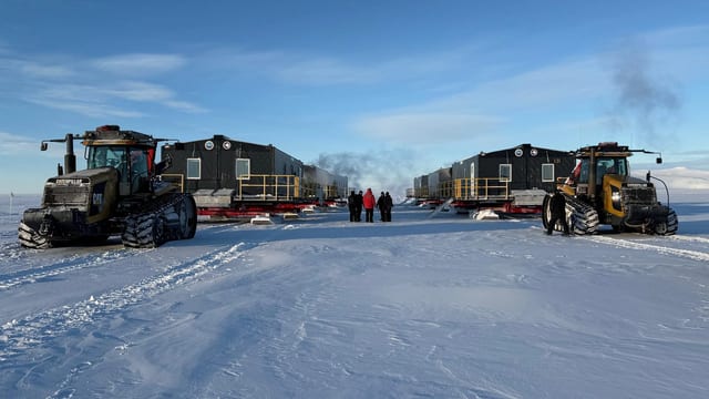 Interlock-clad Antarctic research modules on snow with tracked tractors and expedition personnel