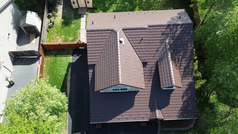 A colonial-style home with a brown metal roof in a wooded suburban area
