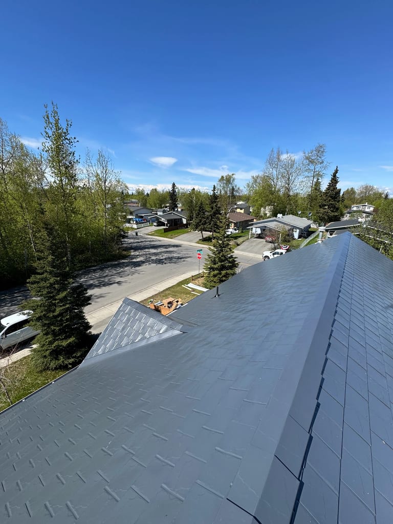 A modern single-family home with a grey metal roof and a blue sky.