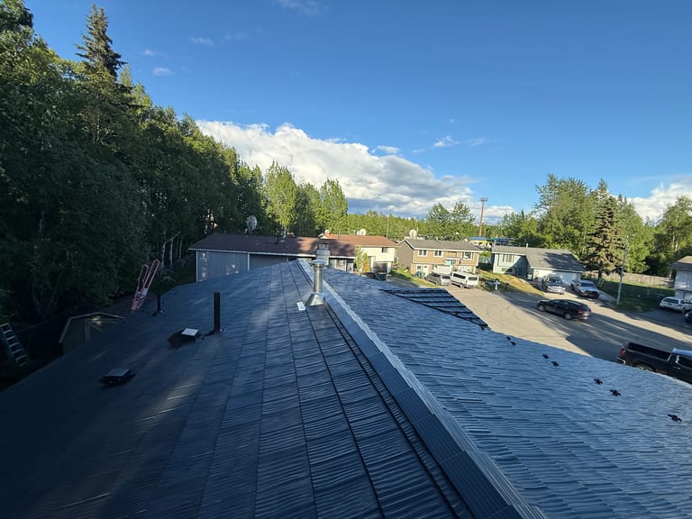 A finished metal roof in a ranch style home with lush greenery and a blue sky
