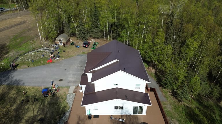 A white house with a brown metal roof in a forested, rural setting.