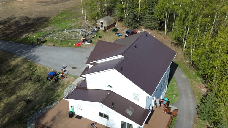 A white ranch-style home with a brown metal roof, situated in a forested rural area.