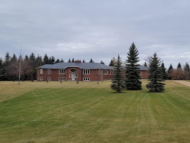 Deep Charcoal Interlock Slate aluminum roof on a red brick home with a grey metal roof in a forest clearing, Westlock, Alberta
