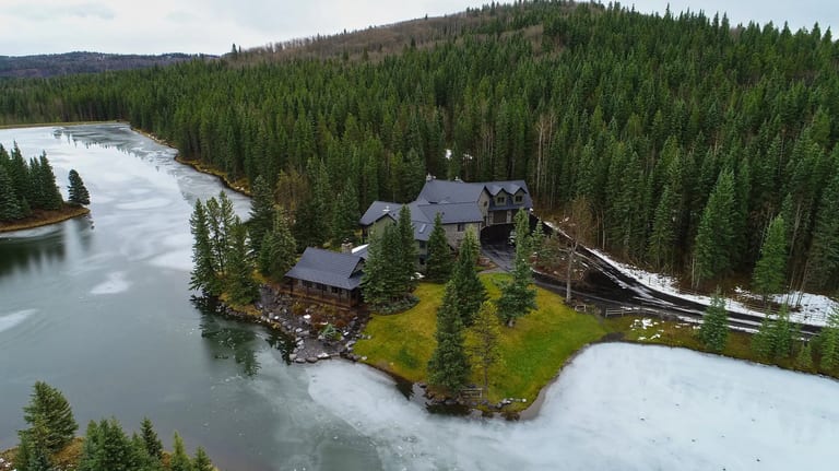 Aerial view of a chalet-style home on a lakeside peninsula in Bragg Creek AB featuring black Interlock aluminum shake metal roofing with complex multi-gable design.