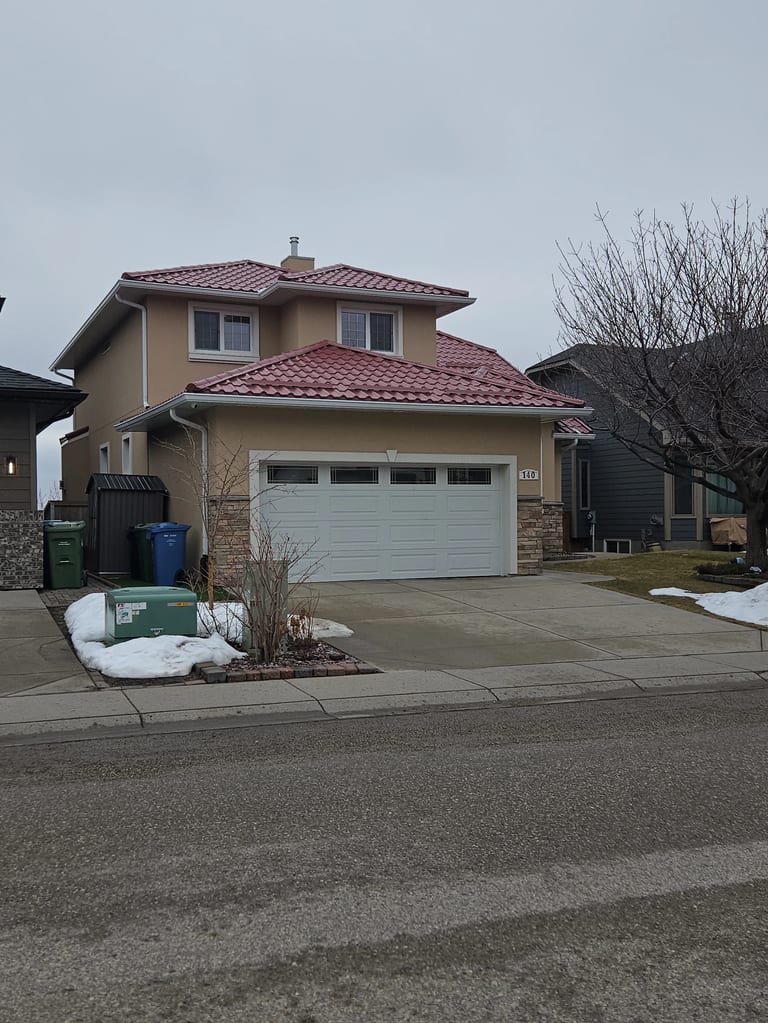 Tile Red Interlock Tile aluminum roof on a tan two-storey home with a red metal roof in an urban, Calgary, Alberta