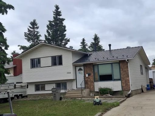 Deep Charcoal Interlock Cedar Shingle aluminum roof on a two-storey home with a metal roof among tall evergreens, Grande Prairie, Alberta