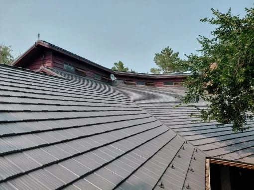Musket Grey Interlock Shake aluminum roof on a red two-storey home with dormers among tall trees, Warner, Alberta