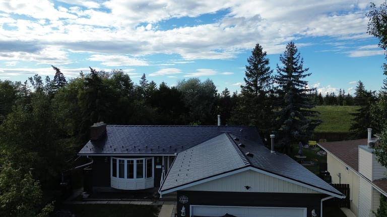 Black Interlock Slate aluminum roof on a black metal roof on a white bungalow among tall trees, Edmonton, Alberta