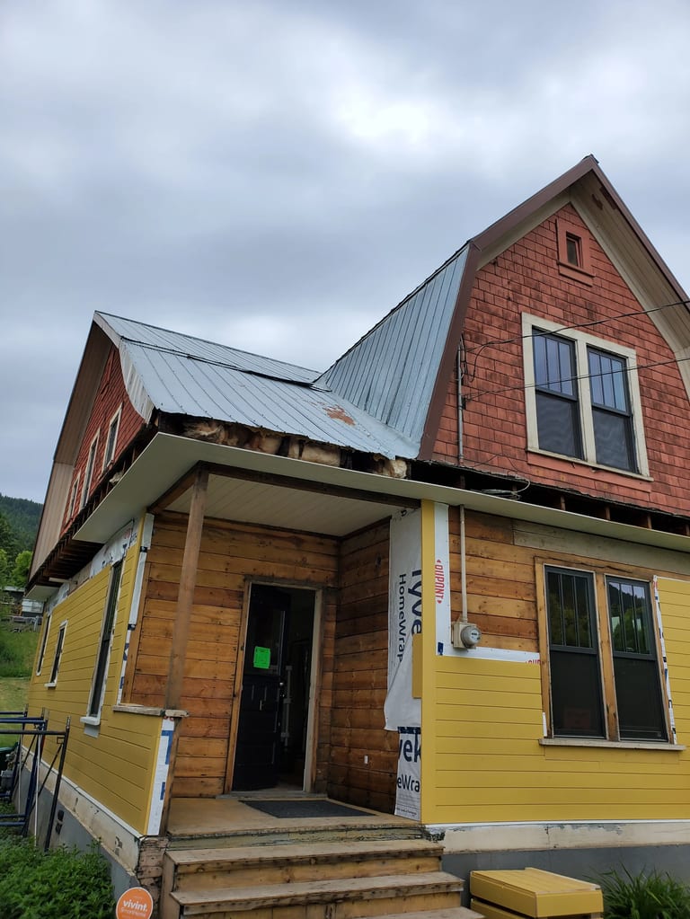 Copper Penny Interlock Cedar Shingle aluminum roof on a yellow cottage with dormers among tall pine trees, Lumby, British Columbia