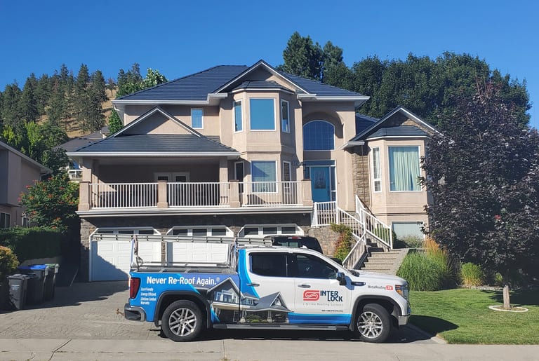 Large two-storey stucco home in Kelowna BC with a complex multi-hip Interlock aluminum slate roof in deep charcoal, featuring multiple valleys and dormers.