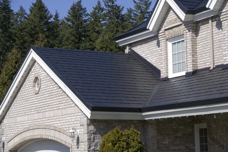 After: Black Interlock Slate aluminum roof on a grey two-storey Craftsman home with dormers among tall, Surrey, British Columbia