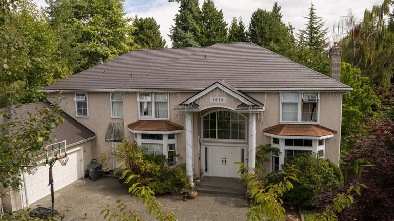 Tudor Brown Interlock Slate aluminum roof on a two-storey Tudor home with dormers among tall trees, Surrey, British Columbia