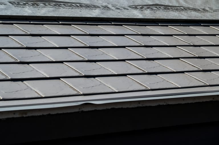Taupe Interlock Slate aluminum roof on a taupe metal roof on a two-storey home among tall pines, Surrey, British Columbia