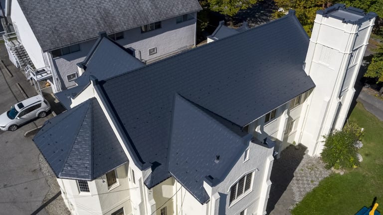 Deep Charcoal Interlock Slate aluminum roof on a white single-family home with a metal roof and tall trees, Vancouver, British Columbia