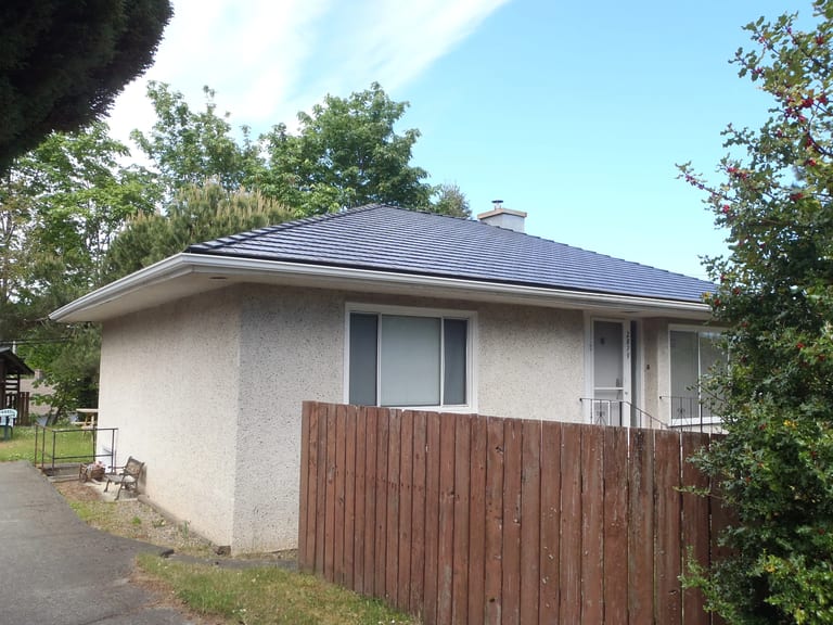 Black Interlock Cedar Shingle aluminum roof on a beige one-storey home with a small chimney and a fence, Chemainus, British Columbia