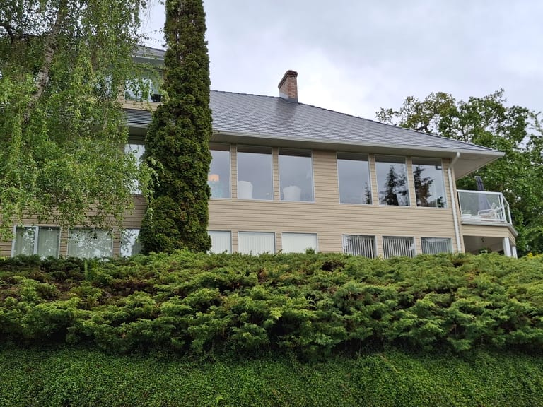 After: Deep Charcoal Interlock Slate aluminum roof on a two-storey home with a metal roof and dormers among tall, Duncan, British Columbia