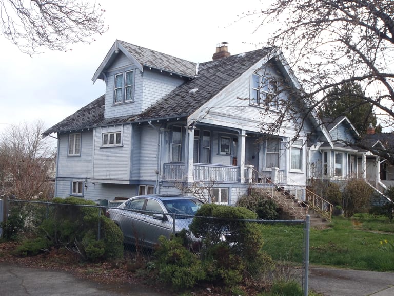 Before: Tudor Brown Interlock Cedar Shingle aluminum roof on a light grey two-storey Tudor home with dormers and a metal, Victoria, British Columbia
