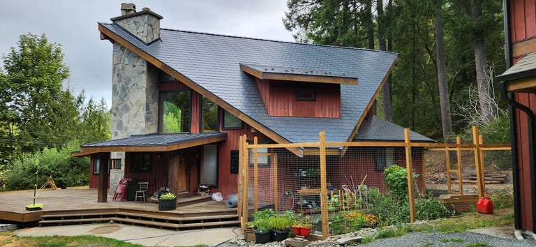 Deep Charcoal Interlock Slate aluminum roof on a red chalet-style home with a metal roof among tall trees, Shawnigan Lake, British Columbia