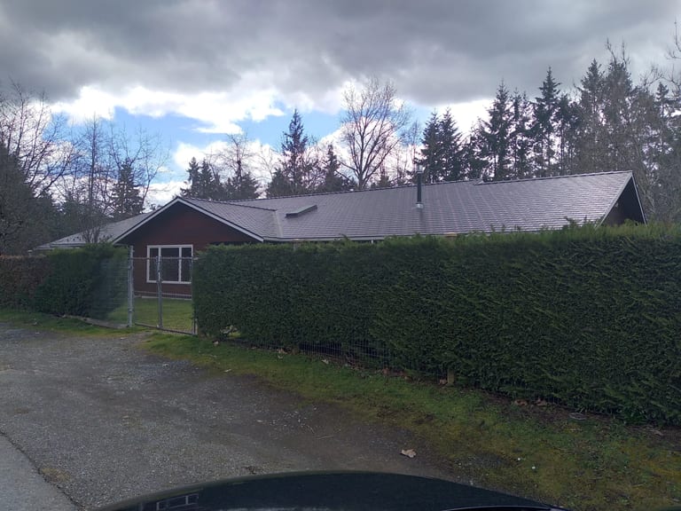 Tudor Brown Interlock Slate aluminum roof on a Tudor brown single-storey home among tall evergreens, Duncan, British Columbia