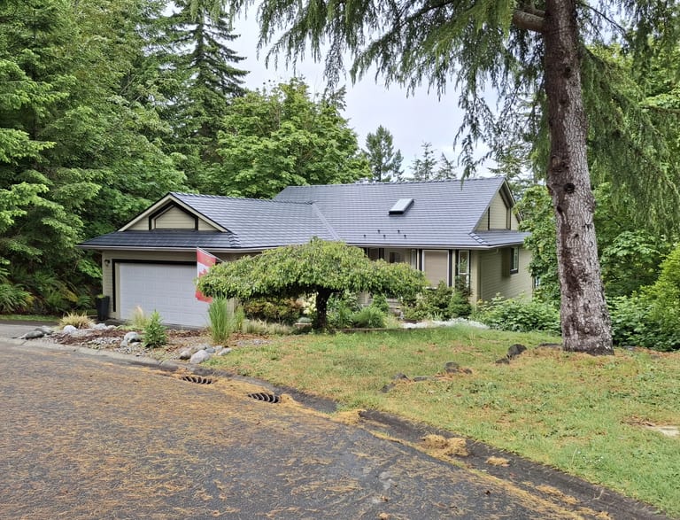 Black Interlock Slate aluminum roof on a tan one-storey home with dormers among tall evergreens, Duncan, British Columbia