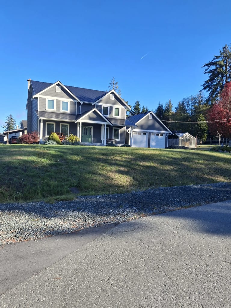 Black Interlock Slate aluminum roof on a grey two-storey home with dormers among tall pines, Sooke, British Columbia
