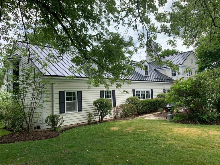 Black Interlock Standing Seam aluminum roof on a white house with a black metal roof among tall trees, Lake Forest, Illinois