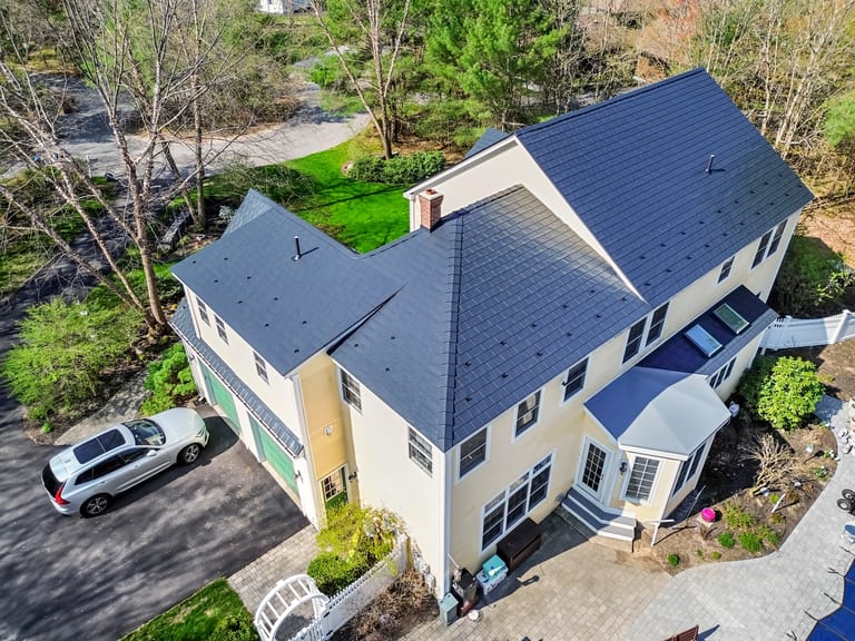 Black Interlock Slate aluminum roof on a cream-coloured two-storey home with dormers in a forested, Brunswick, Maine