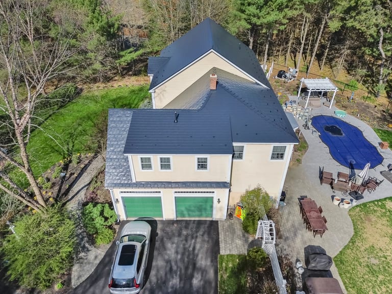 Black Interlock Slate aluminum roof on a beige two-storey home with dormers in a forested setting, Brunswick, Maine