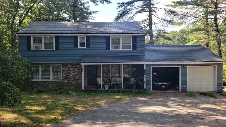 Deep Charcoal Interlock Slate aluminum roof on a dark blue two-storey home with a metal roof among tall, Ipswich, Massachusetts