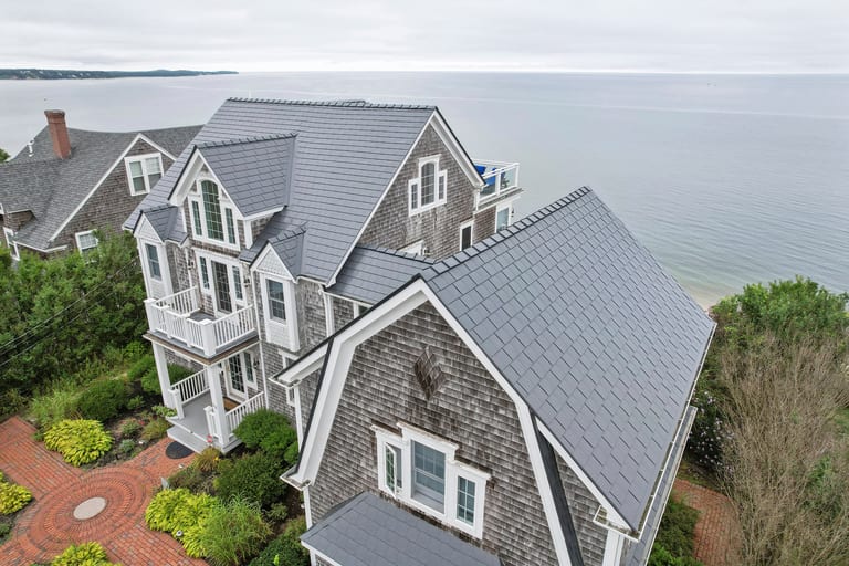 Aerial view of a large coastal shingle-style home in Sagamore Beach, MA featuring a complex Deep Charcoal Interlock aluminum slate metal roof with multiple dormers and valleys.