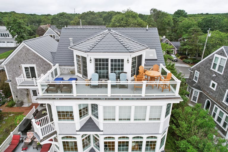 Aerial front view of a 3-story coastal shingle-style home in Sagamore Beach, MA featuring a multi-hip Interlock aluminum slate roof in Deep Charcoal with a rooftop deck.