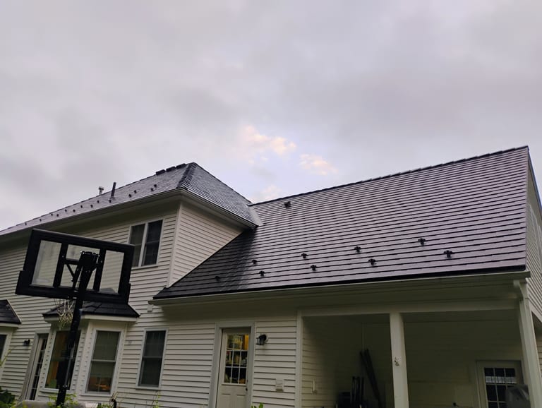 Two-story Colonial home with a complex black Interlock aluminum slate metal roof featuring snow guards, a dormer, and covered rear porch.