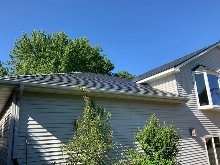 Deep Charcoal Interlock Slate aluminum roof on a grey two-storey home with a metal roof among tall trees, Rochester, Minnesota