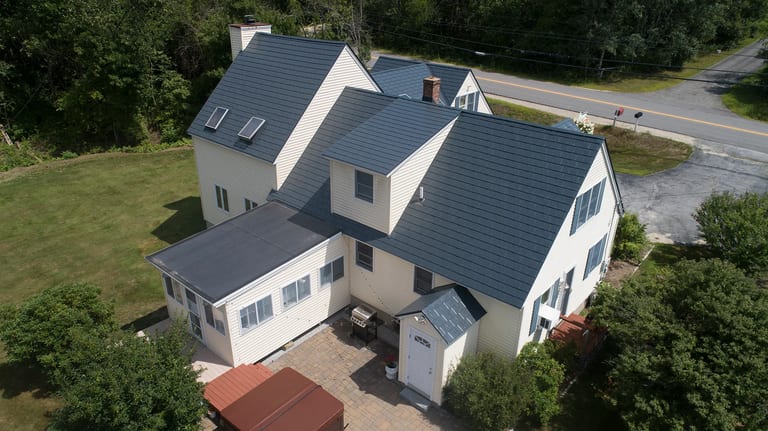 Deep Charcoal Interlock Slate aluminum roof on a white two-storey home with dormers among tall pines, Hooksett, New Hampshire