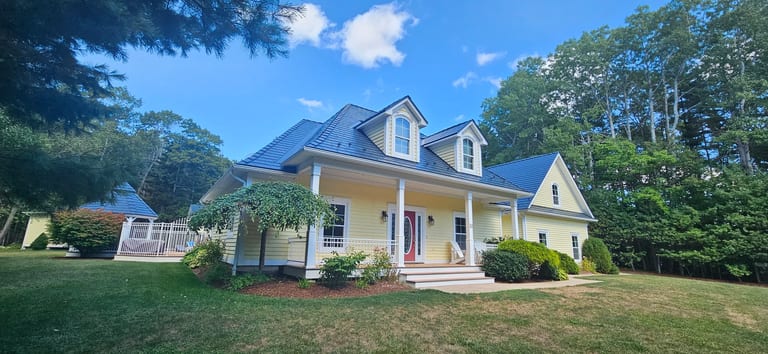 A yellow house with a blue roof, surrounded by greenery