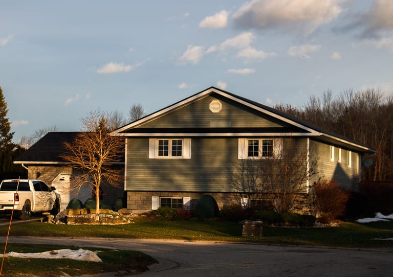 Bi-level single-family home in Wiarton ON with black Interlock aluminum slate metal roofing, simple gable profile, and octagonal roof louver at golden hour.