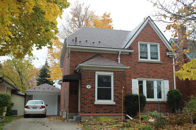 Two-storey red brick Tudor-style home in Kitchener ON with Interlock Colonial Brown aluminum slate metal roofing, hip and gable roof, surrounded by autumn foliage.