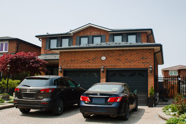 Two-storey brick home in Woodbridge ON with Interlock deep charcoal aluminum slate metal roofing, dormers, and double dark garage doors.