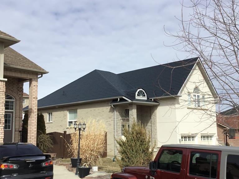 Black Interlock aluminum slate metal roof on a 1.5-storey suburban home in Bradford, featuring a complex hip profile and arched dormer window.