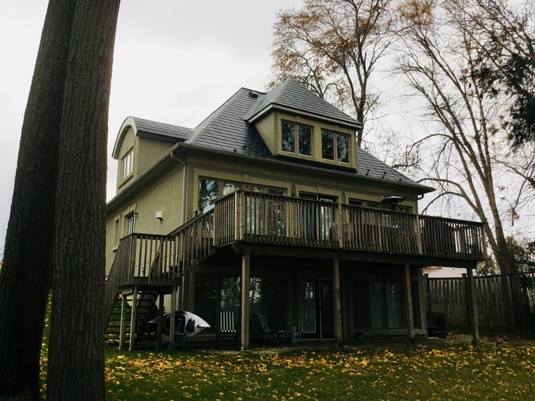 Rear elevation of a 3-storey Victorian home in Orillia ON featuring black Interlock aluminum slate roofing with a central turret, dormer, and large elevated wood deck.