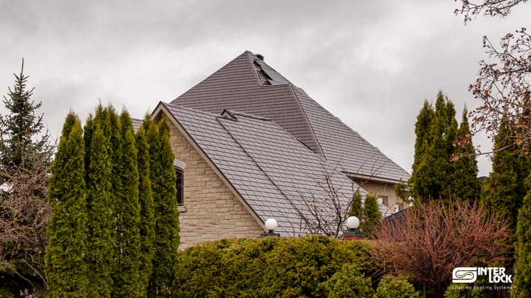 Large Tudor-style stone home in Sudbury ON featuring a steeply pitched multi-hip Interlock aluminum slate roof in Tudor Brown, surrounded by mature evergreens.