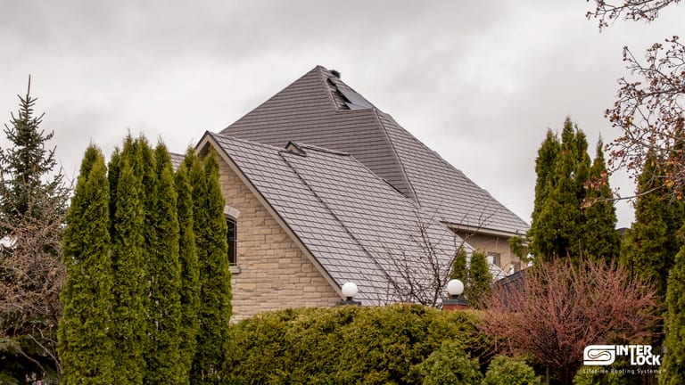 Large two-storey stone home with a steeply pitched multi-hip Interlock aluminum slate roof in Tudor Brown, featuring skylights and complex valleys.