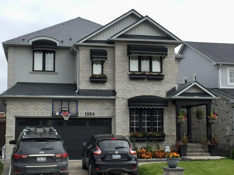 Two-storey craftsman home in Milton ON with black Interlock aluminum slate metal roofing, light grey brick facade, black awnings, and window boxes.