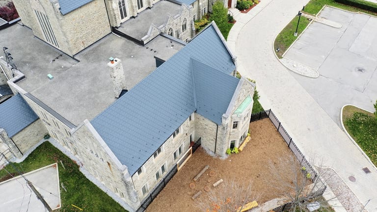 Aerial view of a deep charcoal Interlock aluminum slate metal roof on a historic stone church in Toronto, featuring complex multi-gable geometry and a stone chimney.