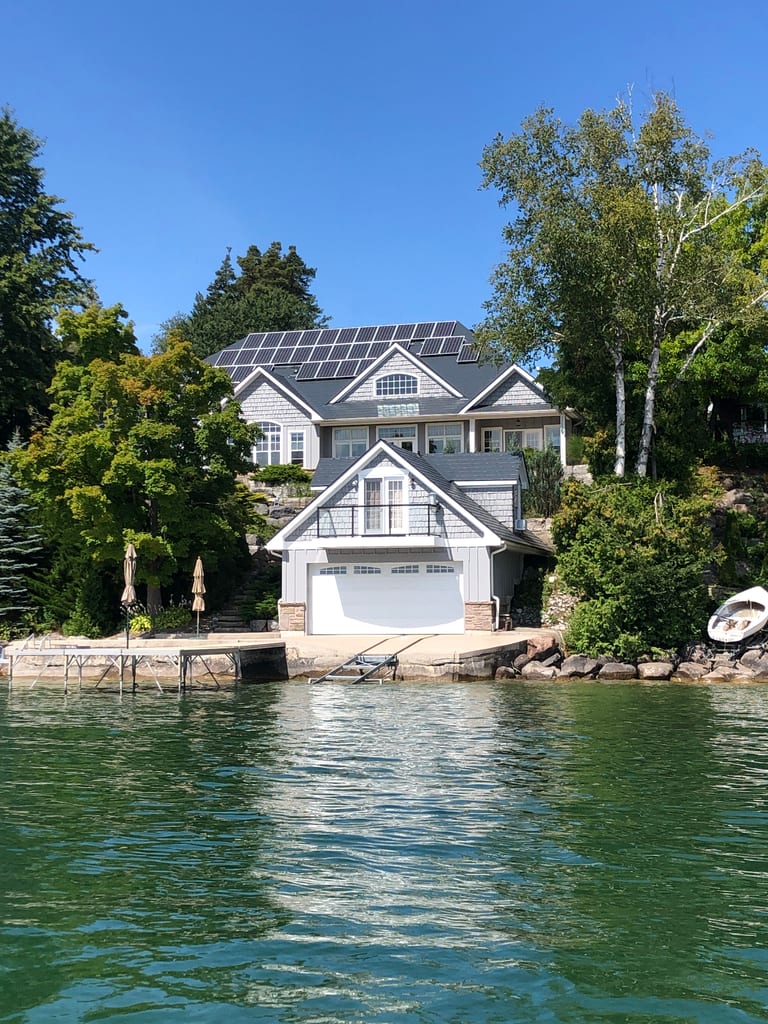 Large Craftsman lakefront home in Shanty Bay, ON with deep charcoal Interlock aluminum slate roof, solar panels, and a boathouse at water's edge.