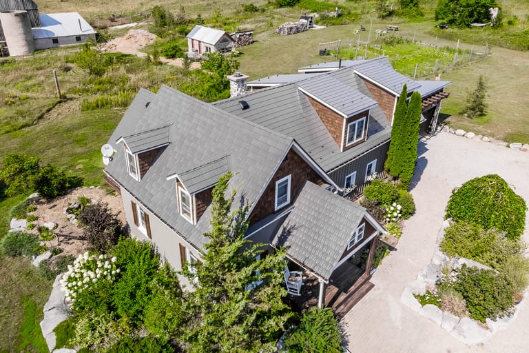 Aerial view of a complex multi-hip Interlock aluminum cedar shingle roof in Weathered finish on a rural Craftsman-style two-storey home in Midland, ON.