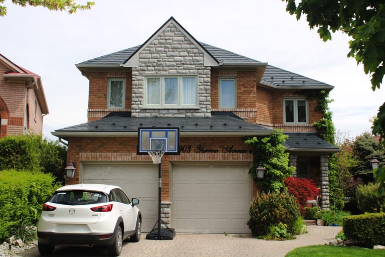 Two-storey brick suburban home in Mississauga with black Interlock aluminum slate metal roofing, complex multi-hip profile, and stone-accented front dormer.